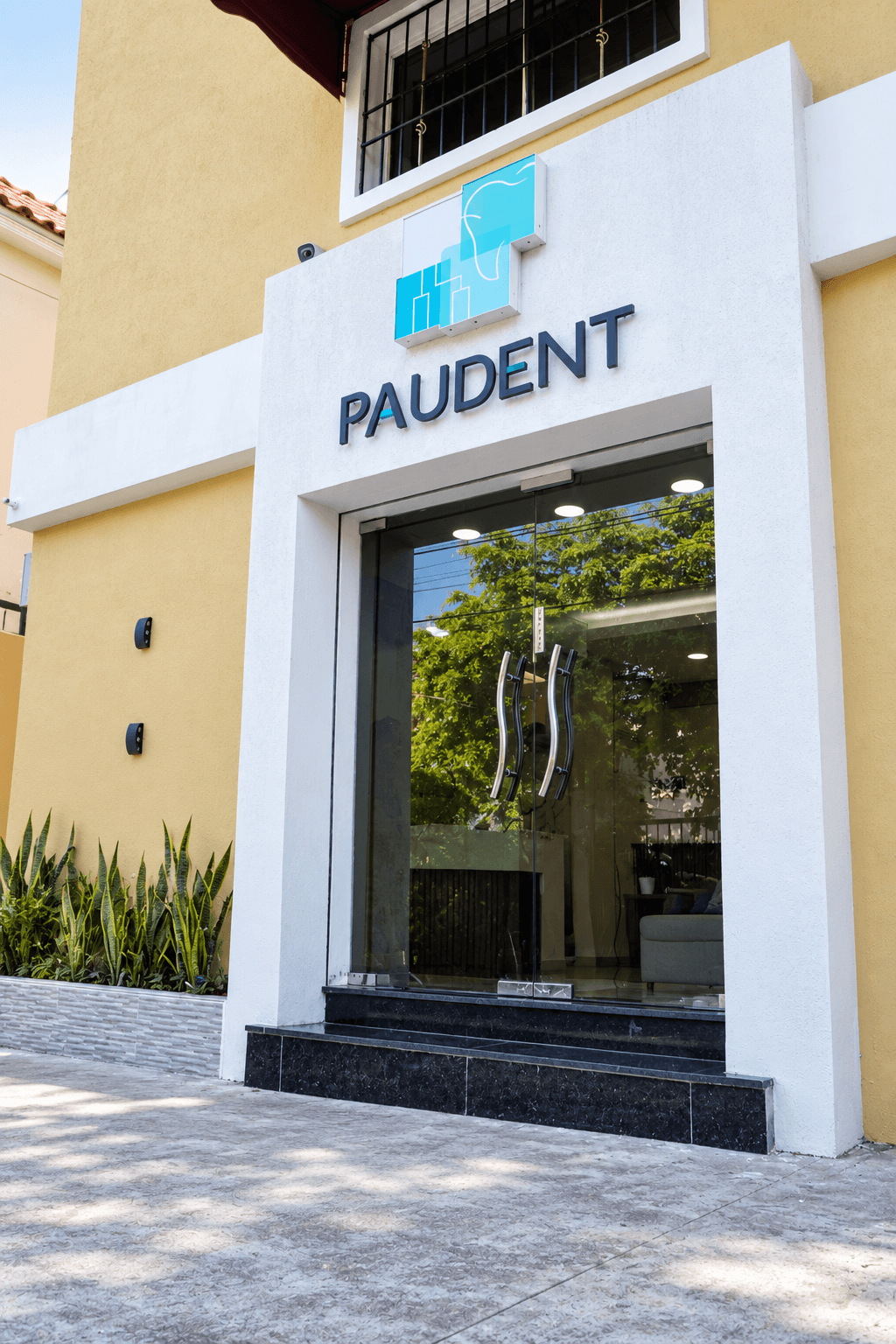 Entrada exterior de PAUDENT con su rótulo, puertas de cristal y escalones de acceso.